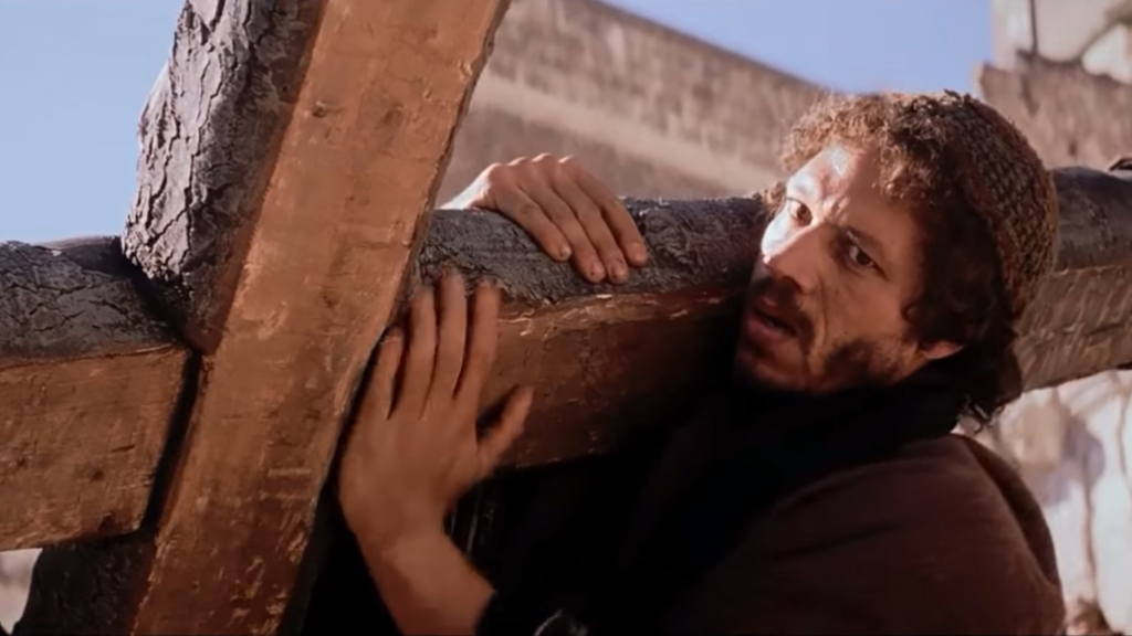 Szymon dźwiga krzyż Jezusa | Kadr z filmu "Pasja" Mela Gibsona