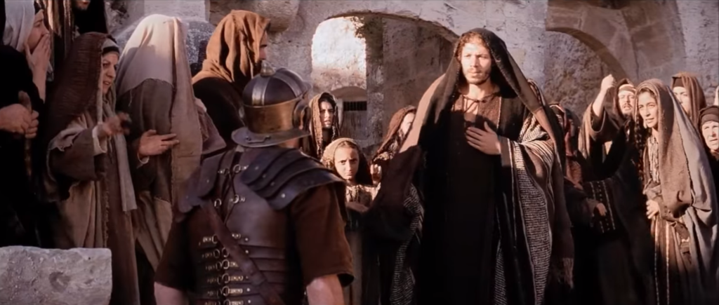 Żołnierz rozkazuje Szymonowi pomóc dźwigać krzyż Jezusa | Kadr z filmu "Pasja" Mela Gibsona
